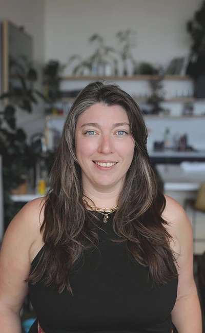 Liz O'Brien, founder of Driftmore Consulting, smiling in a bright room with plants on shelves behind her